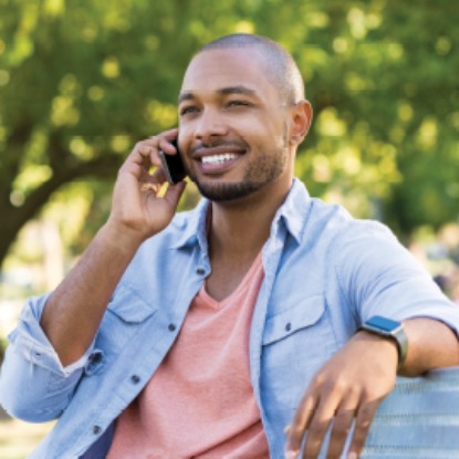 Young man sitting on a park bench, smiling while talking on his cell phone