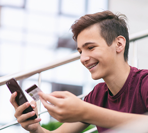 Young man sitting on outside stairs, smiling while holding his debit card and cell phone,