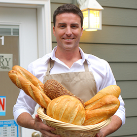 Business owner holding a basket of bread in front of his bakery