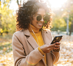 Young female with sunglasses on, smiling while looking at her cell phone.