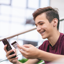 Young male smiling while holding a debit card and cell phone