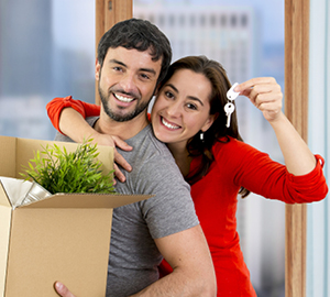 Young couple holding a moving box and keys to their new house.