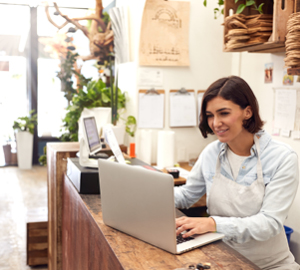 Businesswoman wearing a white apron using her laptop at her store