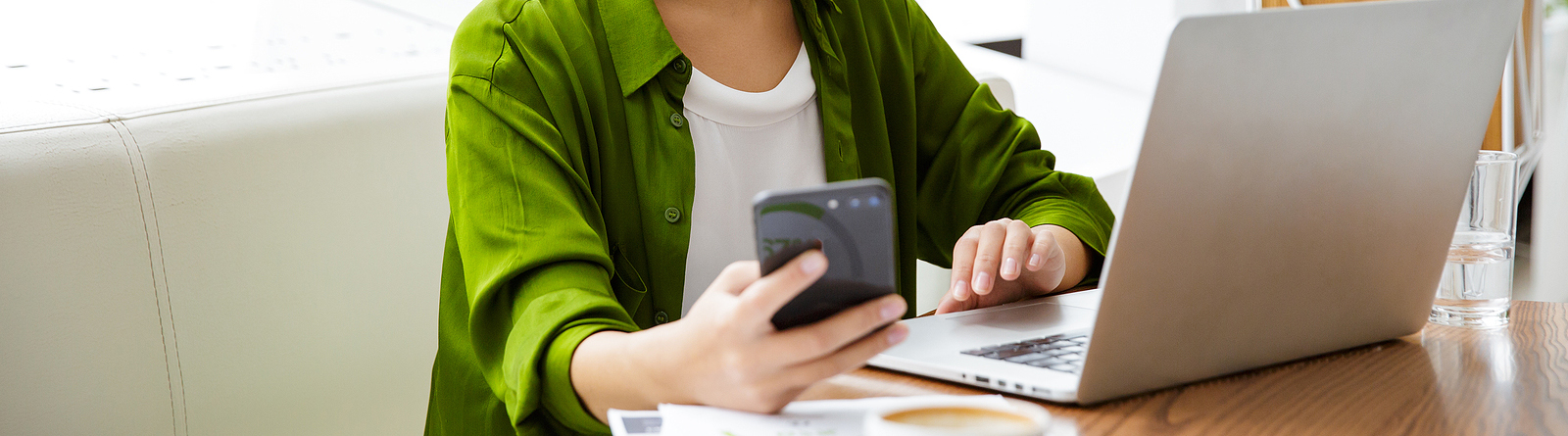 Woman in a green shirt holding a cell phone and using her laptop
