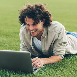 Young man laying on the ground smiling while working on his laptop