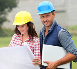 Woman and man in hard hats holding blueprints.