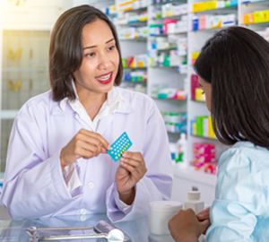 Pharmacist discussing medication with a customer. Shelves of medication are in the background.