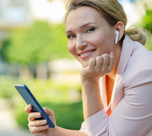 Mature woman sitting outside smiling as she uses her cell phone