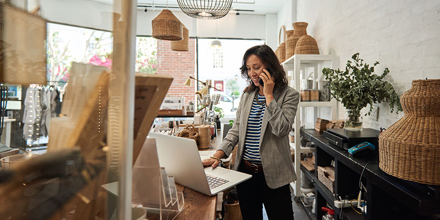 Shop owner looking at laptop - Buy a Business Loan